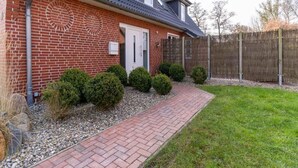 A residential house with a brick exterior, a front door, a small garden with a gravel pathway, and a wooden fence. - Ferienwohnung Deichblume (St. Peter-Ording)