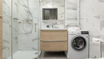 Un baño moderno con cabina de ducha de vidrio, lavadora integrada y tocador de madera.