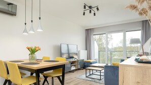 A modern living room with a dining area, large windows, and a flat-screen TV. - Apartment With a View of the River, Pool and Sauna (Dziwnów)