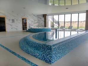 A modern indoor swimming pool with a blue mosaic design, surrounded by lounge chairs and a large window offering a view of the outdoors. - Apartment With a View of the River, Pool and Sauna (Dziwnów)