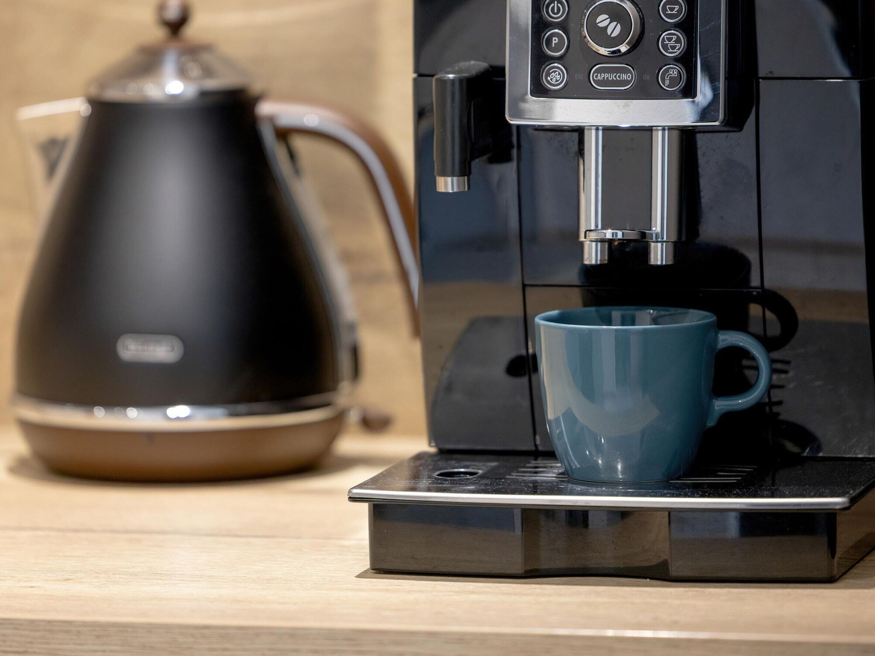 Una cafetera con una taza azul sobre su base, un hervidor negro y un panel de control con botones y una pantalla.