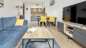 A modern living room with a blue sofa, a wooden coffee table, and a flat-screen TV. - Apartment With a View of the River, Pool and Sauna (Dziwnów)