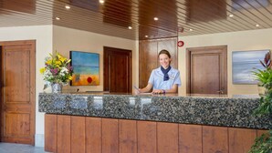 A reception desk with a receptionist, wooden doors, a painting, and a vase of flowers. - Aparthotel Tossa Park-formerly TUI Ferienhaus (Tossa de Mar)