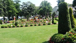 Un giardino curato con siepi ordinate e aiuole fiorite, circondato da alberi e edifici.
