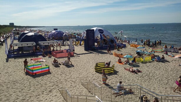 Una spiaggia affollata con tende, sedie a sdraio e ombrelloni.