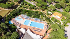 Luchtbeeld van een resort met diverse zwembaden, ligbedden en weelderige begroeiing.