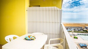 Een balkon met een witte tafel en stoelen, een witte radiator en uitzicht op het strand en de oceaan.