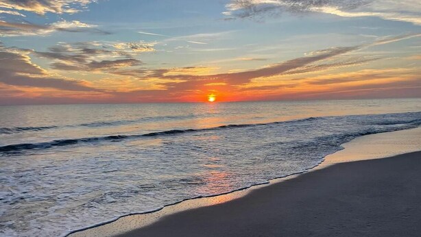 Ein Strand mit sanft anschwellenden Wellen und einem Sonnenuntergang im Hintergrund.