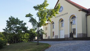 Ein Gebäude mit der Aufschrift "SCHLOSSTHEATER" an der Fassade, mit Bogenfenstern und einem roten Ziegeldach.