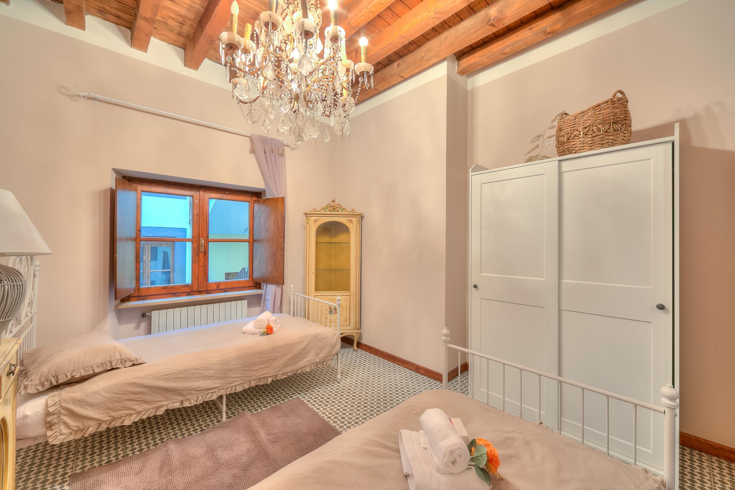 Una habitación con dos camas, un candelabro, un ventanal, un radiador y un armario.