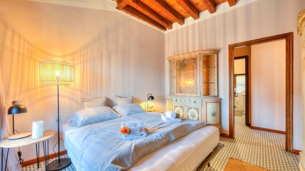A bedroom with a large bed, bedside lamps, a round table with a lamp, and a cabinet with a mirror. - Laetitia Historic Center Fantastic View L (Salò)