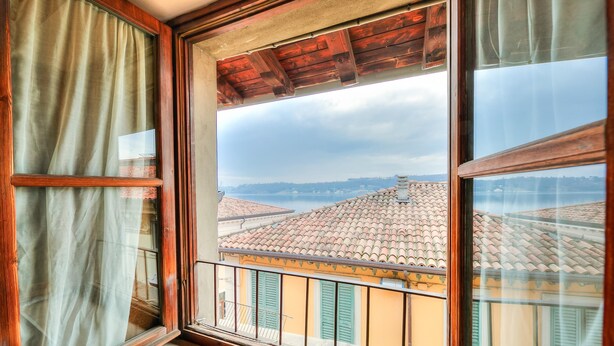A window with a view of terracotta-roofed buildings and a wooden ceiling. - Laetitia Historic Center Fantastic View L (Salò)
