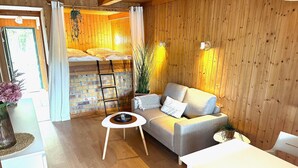 A cozy room with a wooden interior, a sofa, a small table, and a bed with a brick wall behind it. - Bootshaus, Mirow (Mirow)