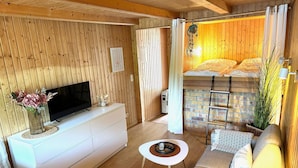 A cozy room with a TV on a white dresser, a sofa, a small table, and a bed with a wooden headboard. - Bootshaus, Mirow (Mirow)