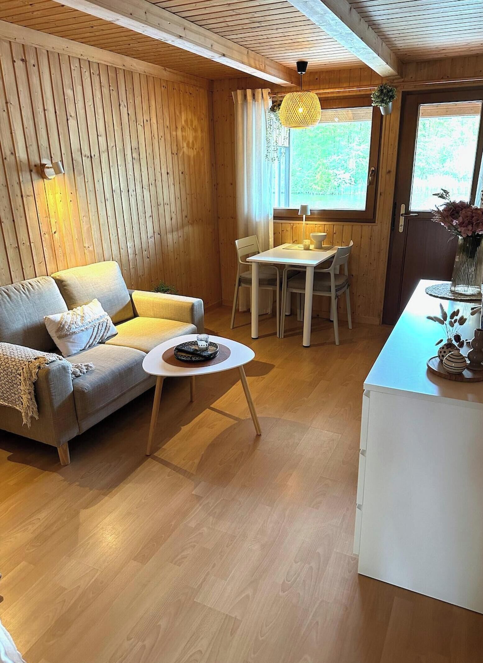 A cozy room with wooden walls, a sofa, a dining table with chairs, and a small kitchen area.