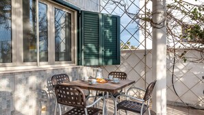 A patio with a table and chairs, a window with green shutters, and a tiled wall.