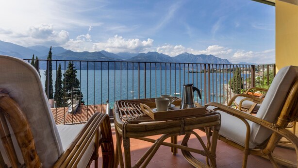 Un balcón con mobiliario de mimbre, una mesa con bandeja y vistas al mar y a las montañas.