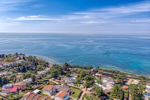 Ett flygbildsbild av ett bostadsområde vid kusten med hus, träd och en fri utsikt över havet.