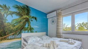 Ein Schlafzimmer mit einem Bett, einem Fenster, einer Klimaanlage und einem tropischen Wandbild.