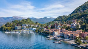 A lakeside town with buildings, a marina, and mountains in the background. - Cedar House Villa Few Minutes From Lake (Angera)