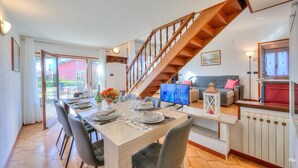 A dining area with a wooden staircase, a sofa, and a dining table set for four. - Cedar House Villa Few Minutes From Lake (Angera)