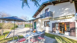 A modern house with a patio, outdoor dining set, and a covered area. - Cedar House Villa Few Minutes From Lake (Angera)
