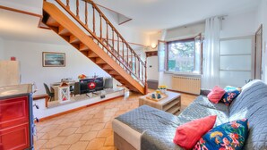 A living room with a wooden staircase, a sofa with colorful cushions, a dining area with a table and chairs, and a red cabinet. - Cedar House Villa Few Minutes From Lake (Angera)