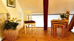A wooden chair with a cushion, a small wooden table with a vase of yellow flowers, and a wicker basket on a wooden floor. - Ferienwohnung Dycke Haus, Zudar (Garz/Rügen)
