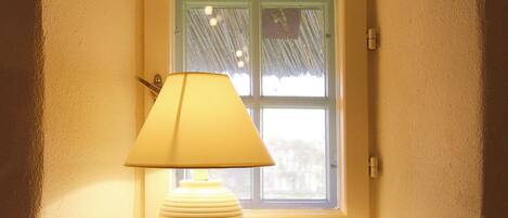 A lamp on a table by a window with two cups.