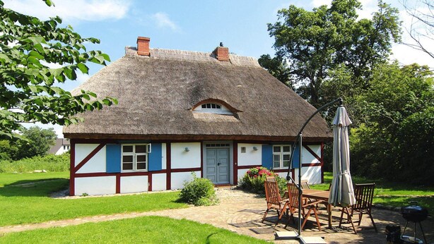 A traditional thatched-roof house with a garden patio, a table with chairs, and a barbecue. - Ferienwohnung Dycke Haus, Zudar (Garz/Rügen)