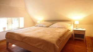 A bedroom with a single bed, two bedside tables with lamps, a window with curtains, and a sloped ceiling. - Ferienwohnung Dycke Haus, Zudar (Garz/Rügen)