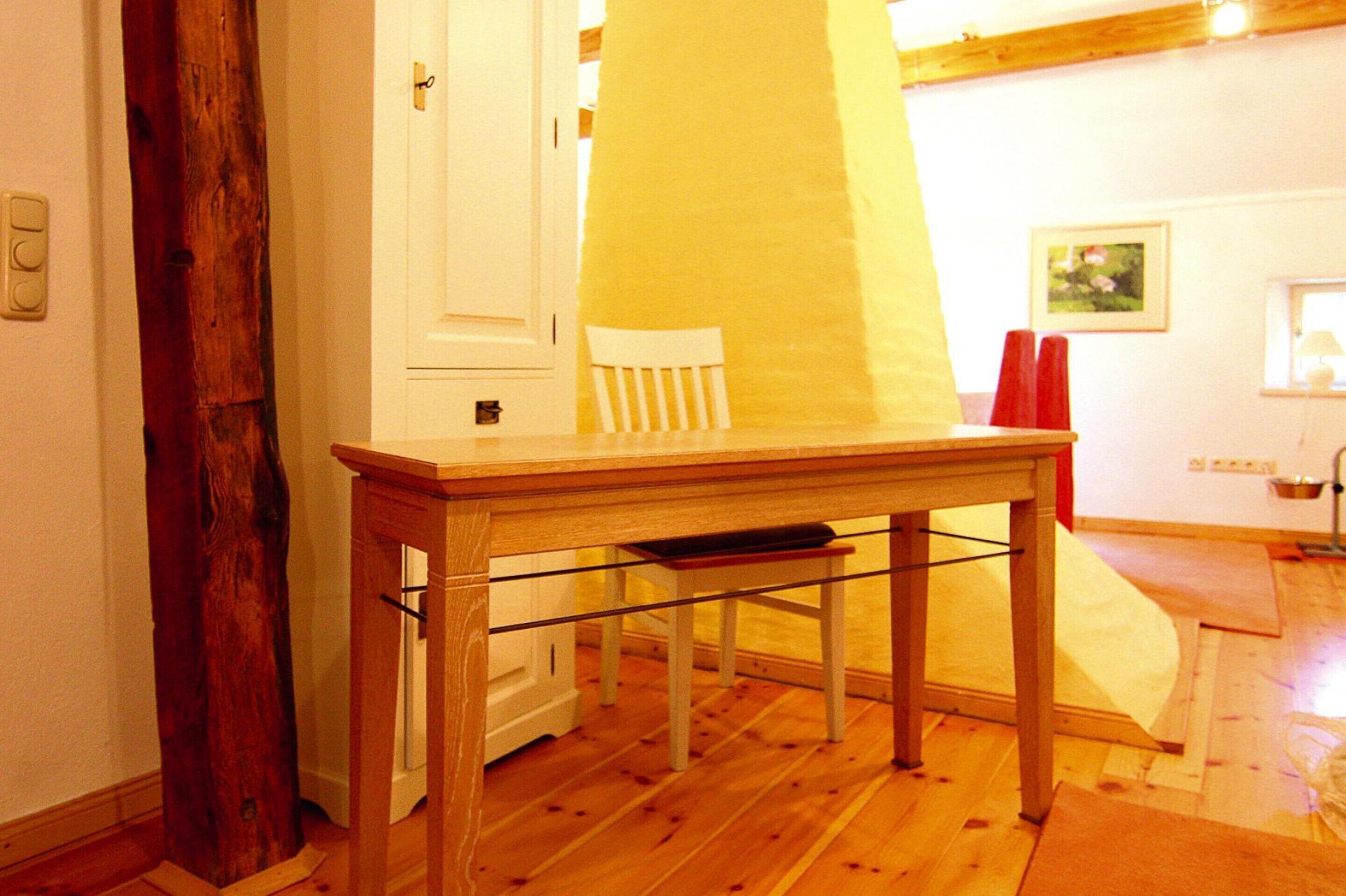 A wooden table with a bench, a white chair, and a yellow wall.