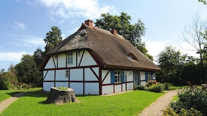 A traditional half-timbered house with a thatched roof, surrounded by a well-maintained garden and a stone pathway. - Ferienwohnung Dycke Haus, Zudar (Garz/Rügen)