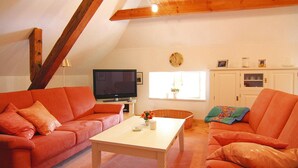 A cozy living room with two orange sofas, a white coffee table, and a television. - Ferienwohnung Dycke Haus, Zudar (Garz/Rügen)