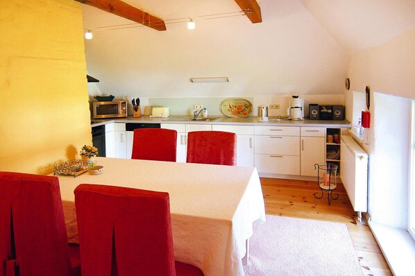 A compact kitchen with white cabinets, a microwave, and a coffee maker. There is a dining area with a table and red chairs. - Ferienwohnung Dycke Haus, Zudar (Garz/Rügen)