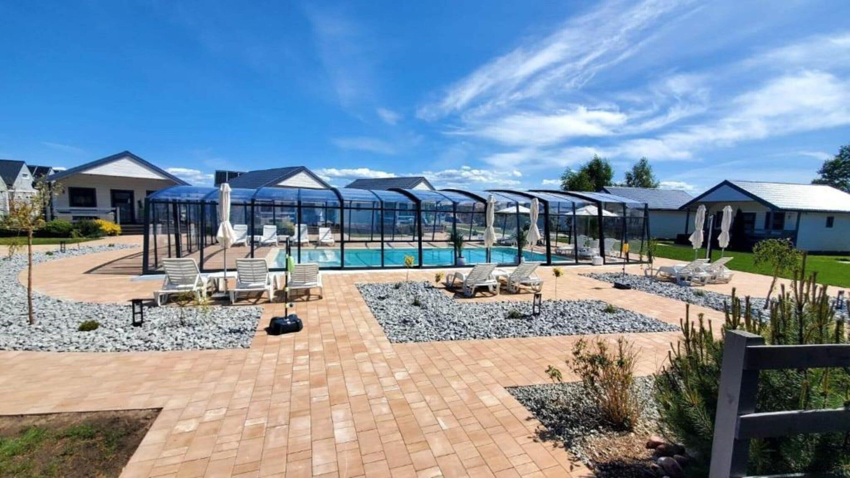 A pool area with sun loungers and a covered seating area, surrounded by a brick patio and a pool.