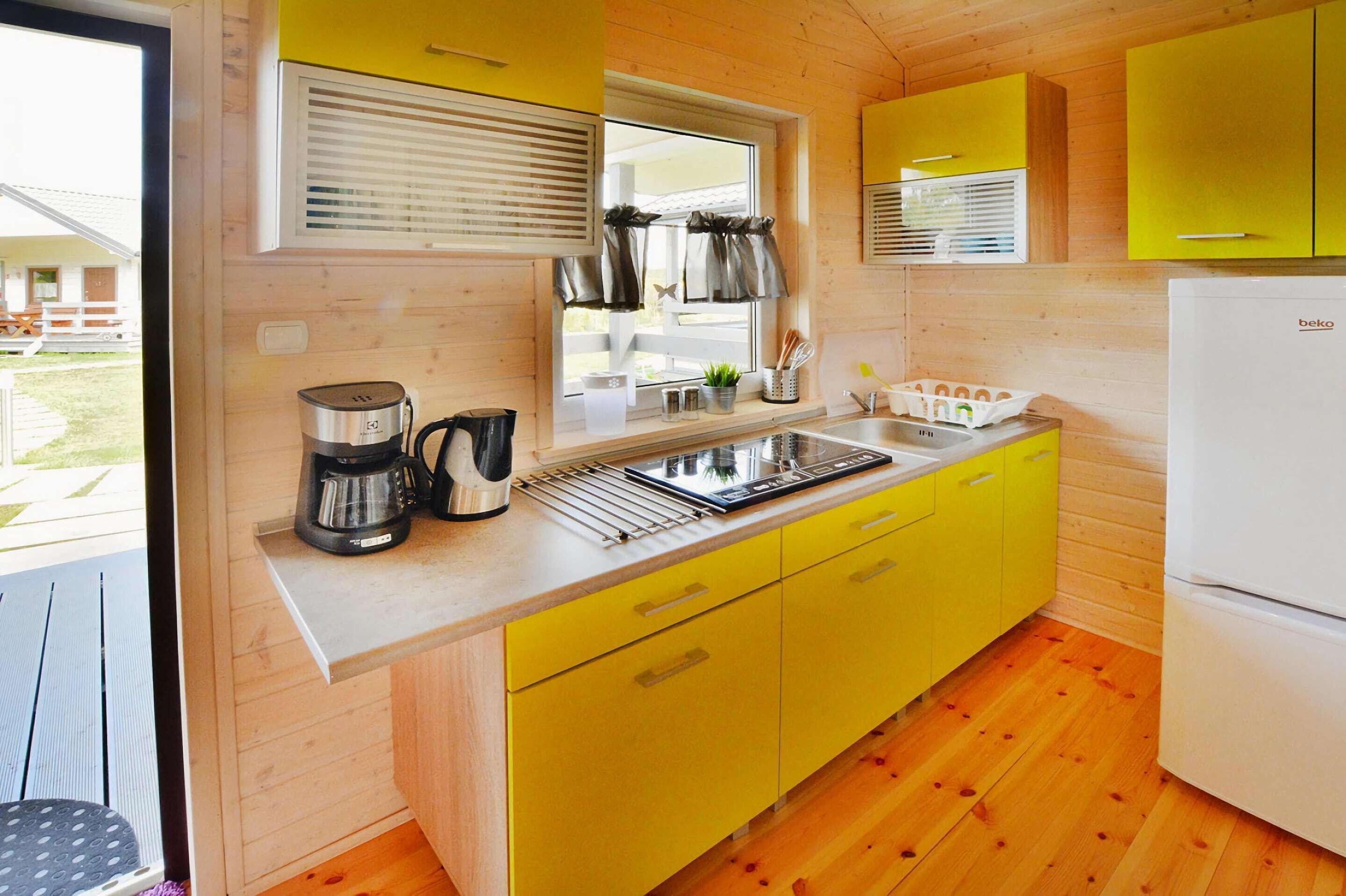 A compact kitchen with yellow cabinets, a sink, a coffee maker, and a window with blinds.