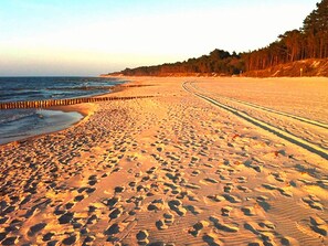 A sandy beach with footprints leading to the ocean, a wooden barrier, and a forested hillside in the background. - Holiday Homes With air Conditioning, Pool, Jacuzzi (Postomino)