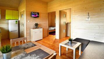 Un acogedor interior de cabaña con revestimiento de madera, un comedor con manteles estampados, una pequeña kitchenette y un televisor montado en la pared.