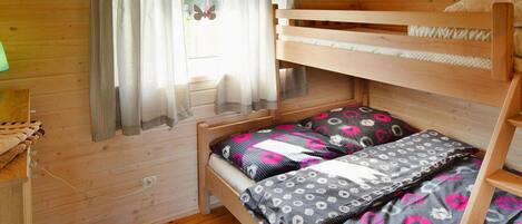 A wooden cabin room with a bunk bed, a window with curtains, and a green rug.