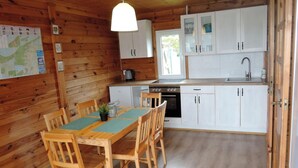 A wooden cabin with a dining table and chairs, a kitchen with white cabinets and a sink, and a map on the wall. - Holiday Home in Kolczewo Near Baltic Sea (gmina Wolin)