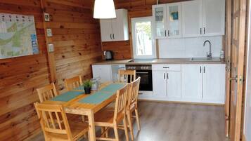 A wooden cabin with a dining table and chairs, a kitchen with white cabinets and a sink, and a map on the wall.