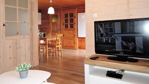 A wooden interior with a television on a wooden stand, a dining area with chairs, and a small table with a plant. - Holiday Home in Kolczewo Near Baltic Sea (gmina Wolin)