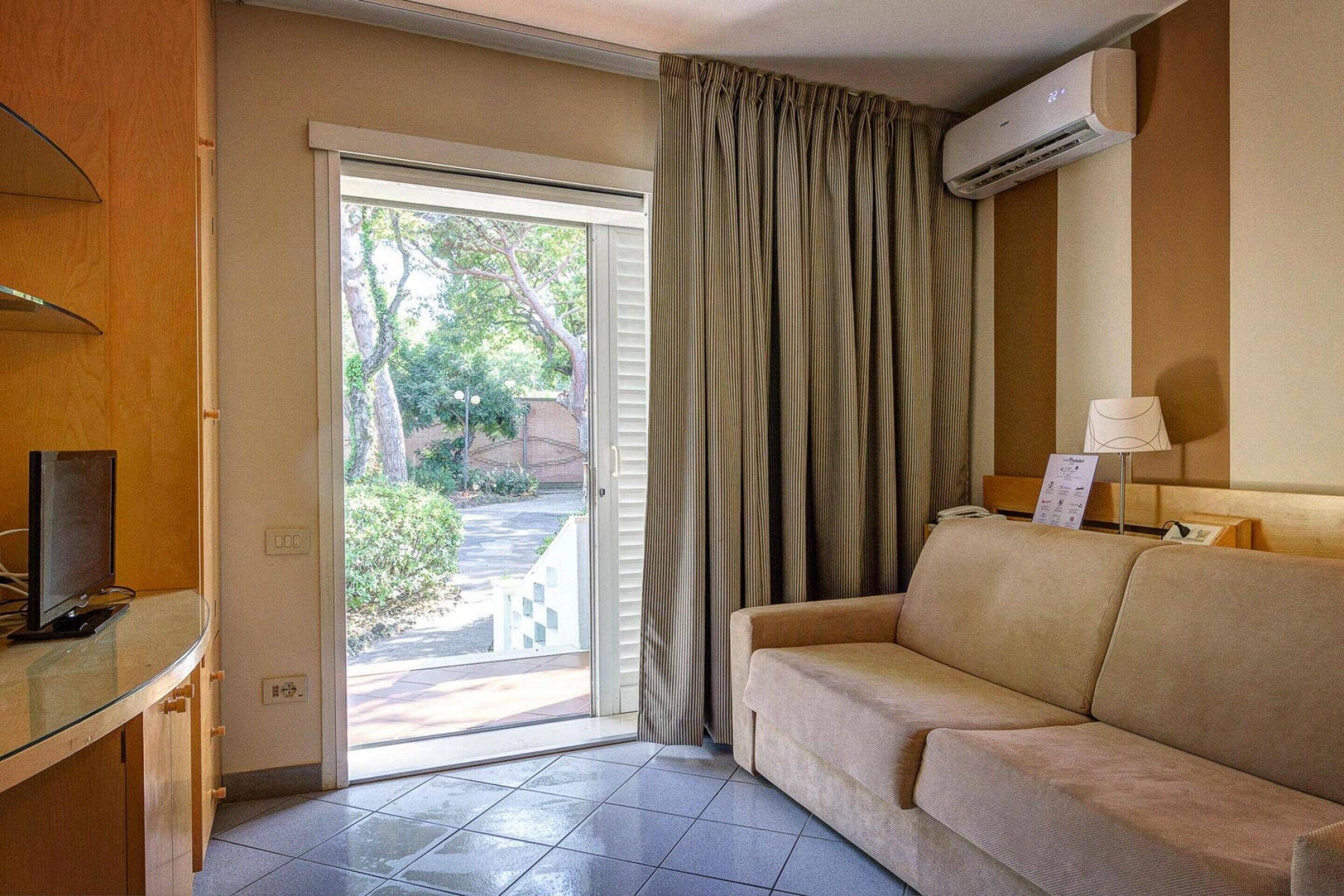Habitación de hotel con sofá, televisión, escritorio y puerta corrediza de vidrio que da a un balcón.
