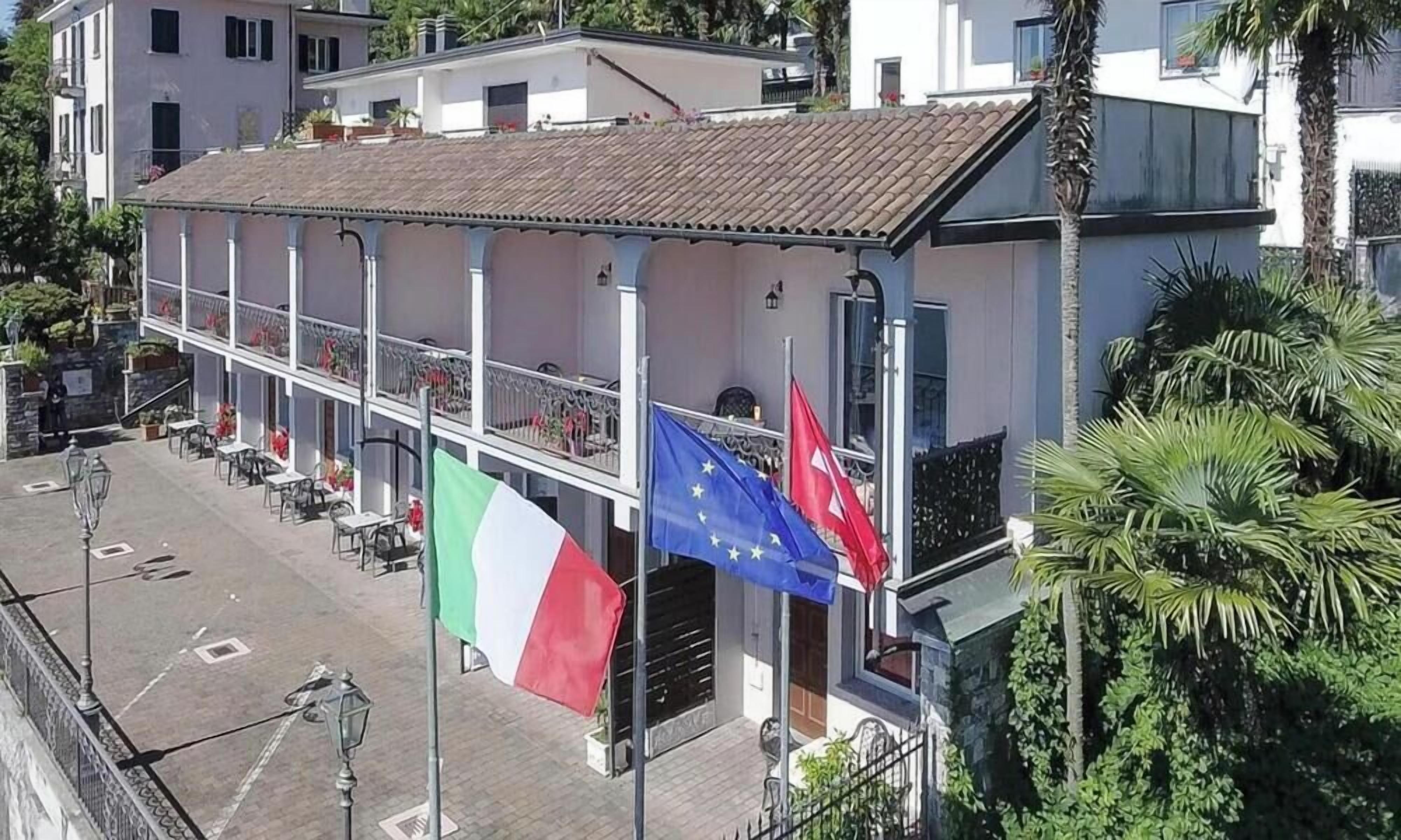 Un bâtiment doté d’un balcon, d’un espace extérieur aménagé pour s’asseoir et de drapeaux.