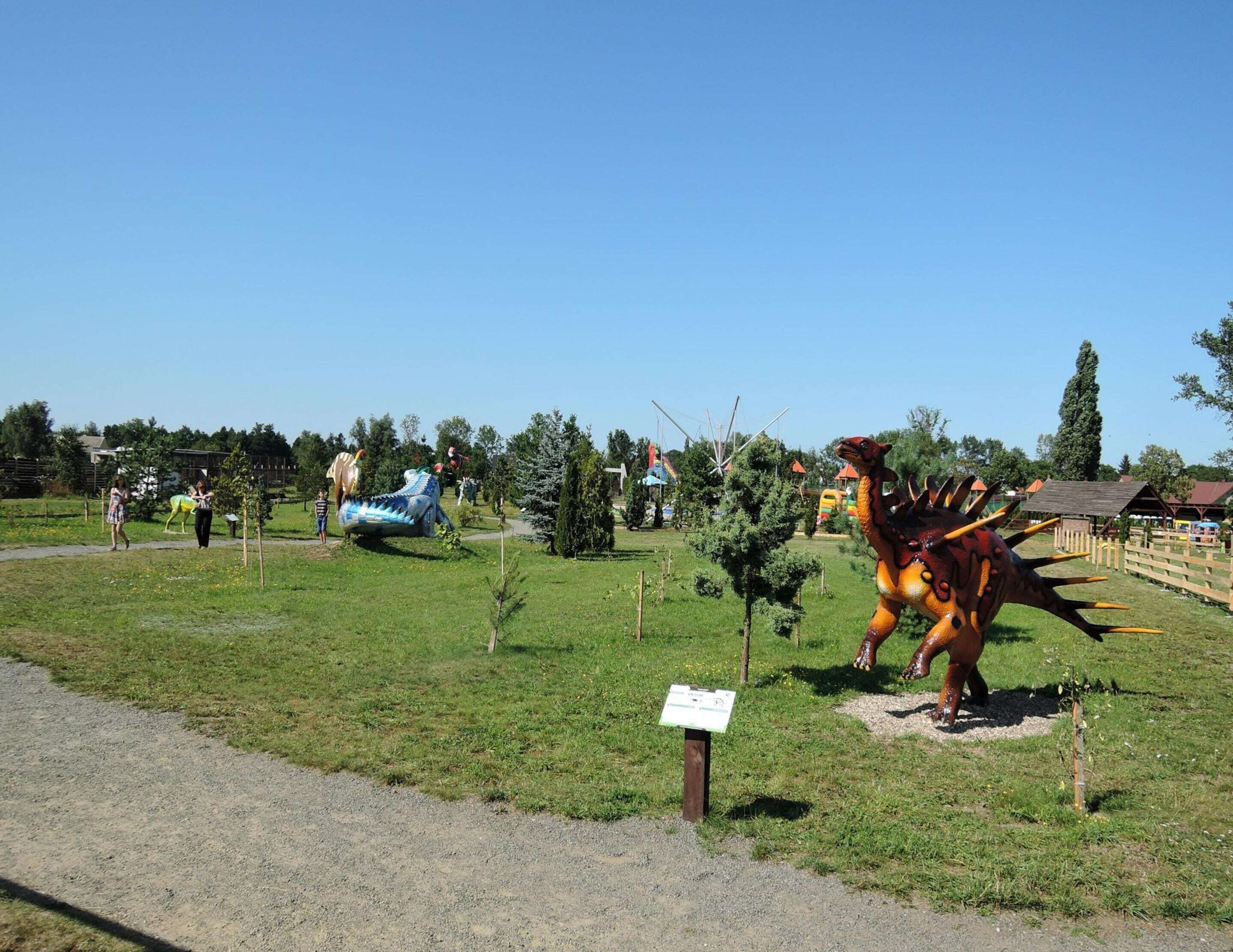 Un parque con una escultura de dinosaurio y una estructura inflable azul.