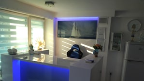 A modern kitchen with a white countertop, a blue-lit bar area, a sailboat painting on the wall, and a refrigerator. - Holiday Home in Dziwnowek Near the Beach (Dziwnów)