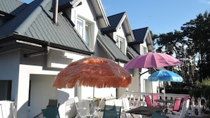 A house with a grey roof, white walls, and a balcony with outdoor furniture and umbrellas. - Holiday Home in Dziwnowek Near the Beach (Dziwnów)