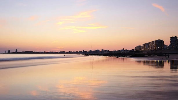 A beach with calm waters reflecting the sunset, a city skyline in the background, and buildings along the shore. - Holiday Home in Dziwnowek Near the Beach (Dziwnów)