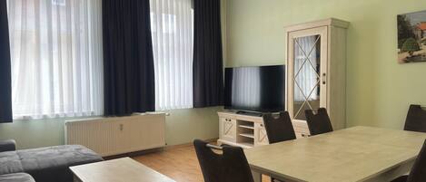 A furnished living room with a sofa, a dining table, chairs, a TV, and a cabinet.
